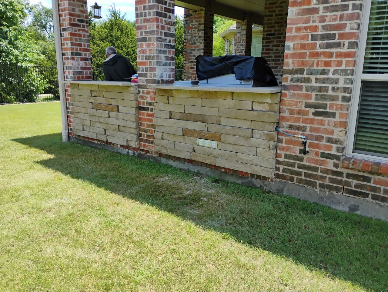 Brick and stone outdoor wall with a covered patio, set in a grassy yard.
