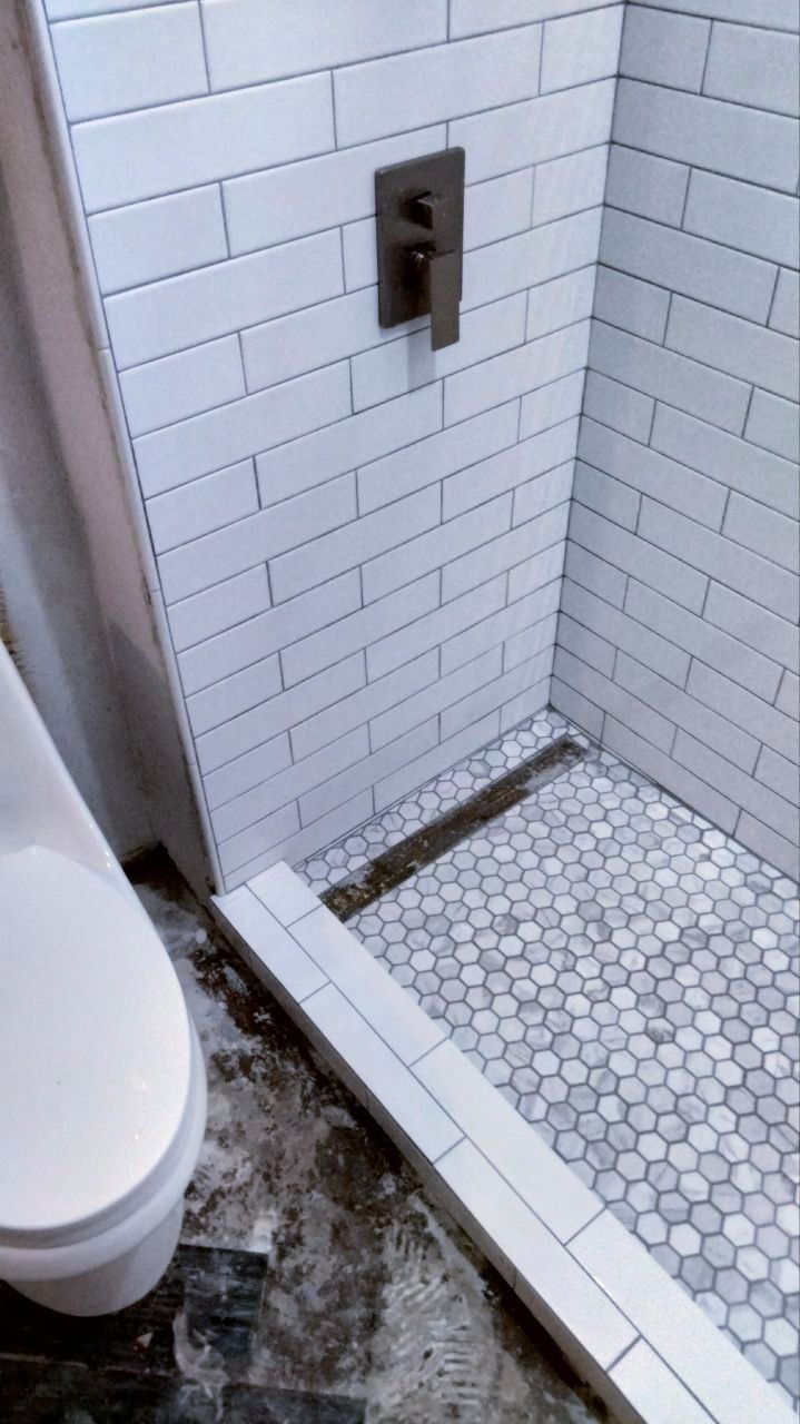 Shower stall with white brick tile walls and mosaic tile floor, next to a white toilet.