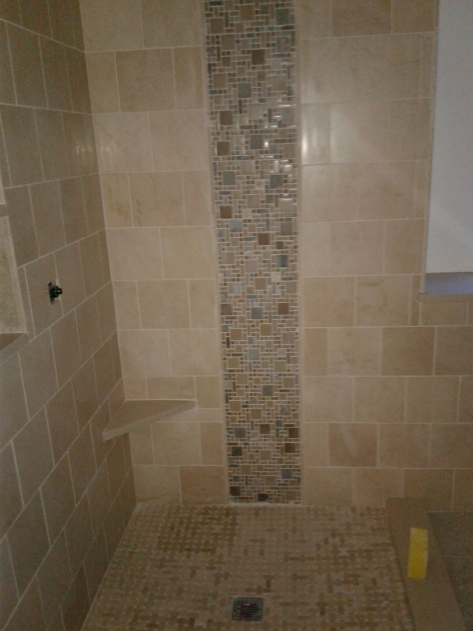 Beige tiled shower with a mosaic tile accent strip and floor, and a built-in shelf.