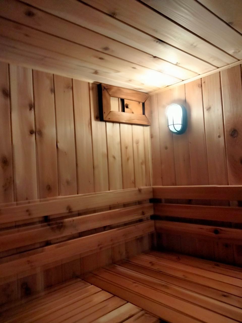 Wooden sauna interior with benches, vent, and light fixture.