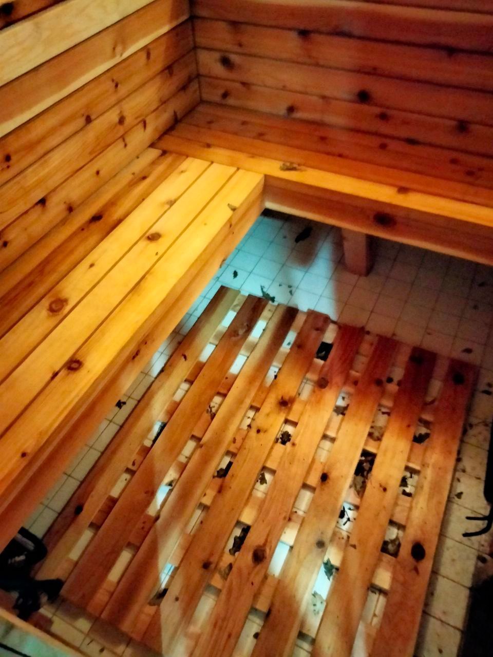 Interior of a wooden sauna with bench seating and a slatted wooden floor mat on tiled floor.