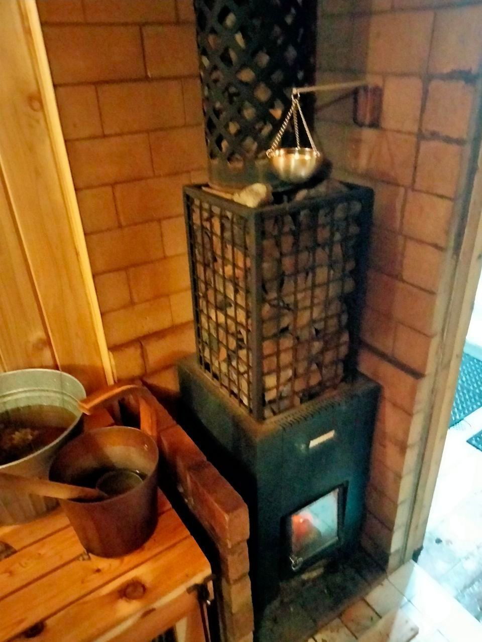 Sauna with stone-filled heater, brick walls, wooden bucket, and metal container for water, interior shot.