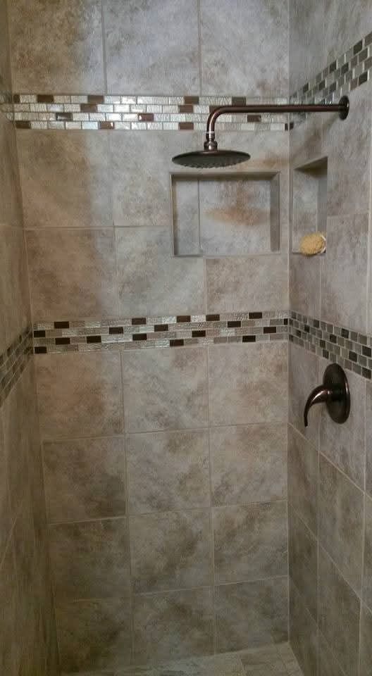 Tiled shower with dark fixtures and mosaic tile accents. Built-in storage.