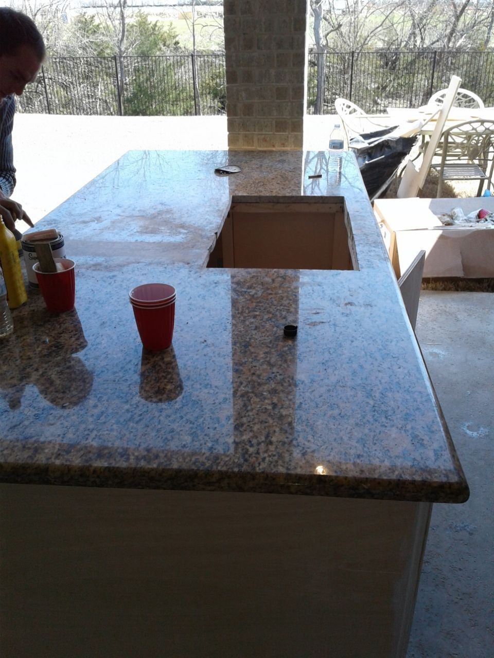 Granite countertop with sink cutout, under construction on an outdoor bar. A person works on the countertop.