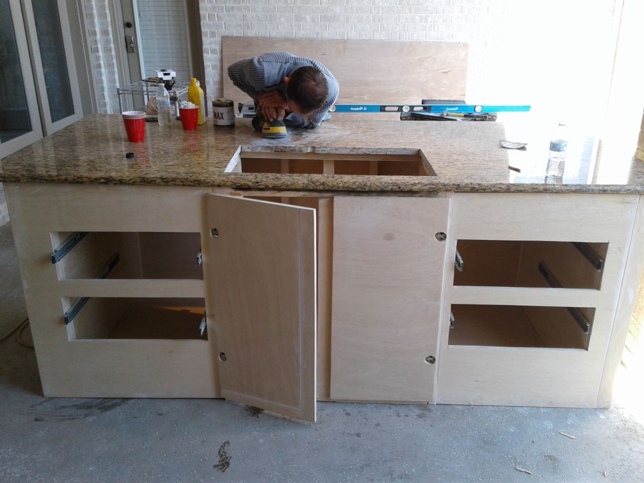 Person sanding a granite countertop on a kitchen island with installed cabinets.