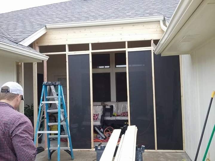 Man working on a screened-in porch with wood framing, ladder, tools, and black screening.