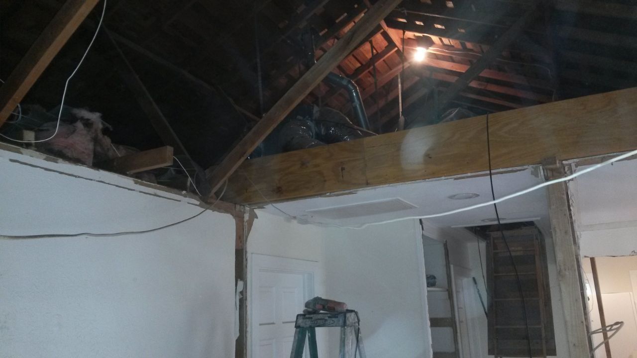 Interior view of a room under construction, with exposed beams, drywall, and a bright overhead light.