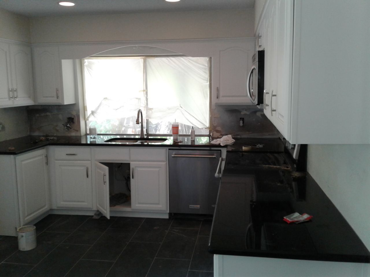White kitchen cabinets with black countertops and a stainless steel dishwasher.