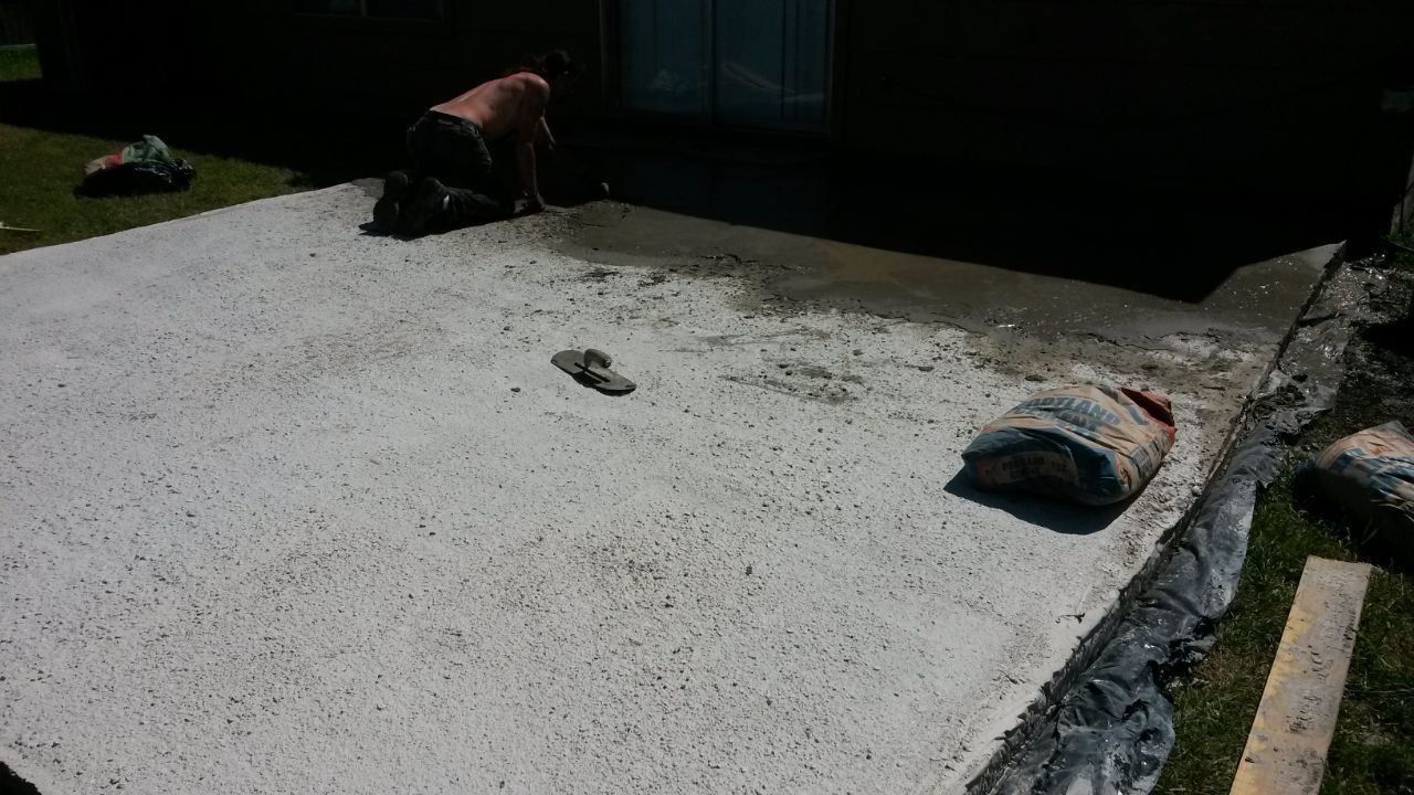Person pouring concrete on a patio. Concrete is spread across a large, rectangular area.