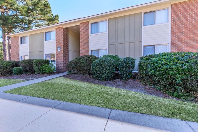 A brick apartment building with a sidewalk and bushes in front of it.