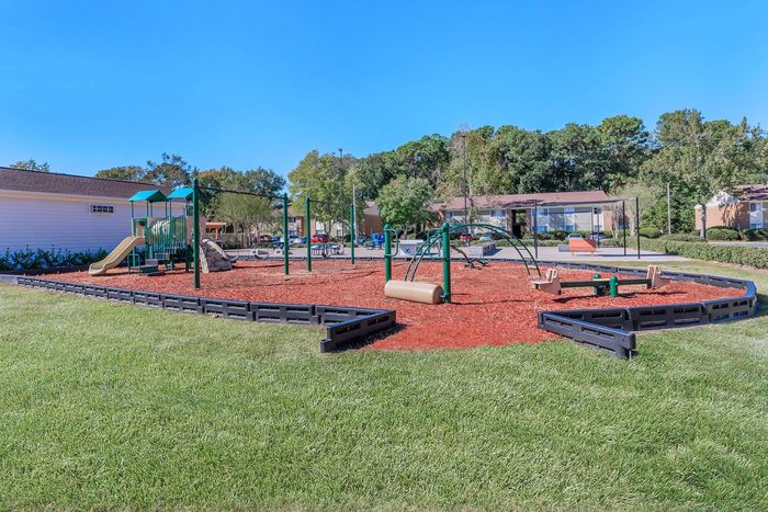 Playground with green equipment, red mulch, and blue sky.