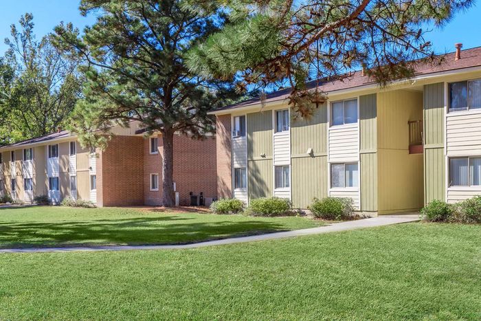 Apartment buildings with green and tan siding, set in grassy area with trees.