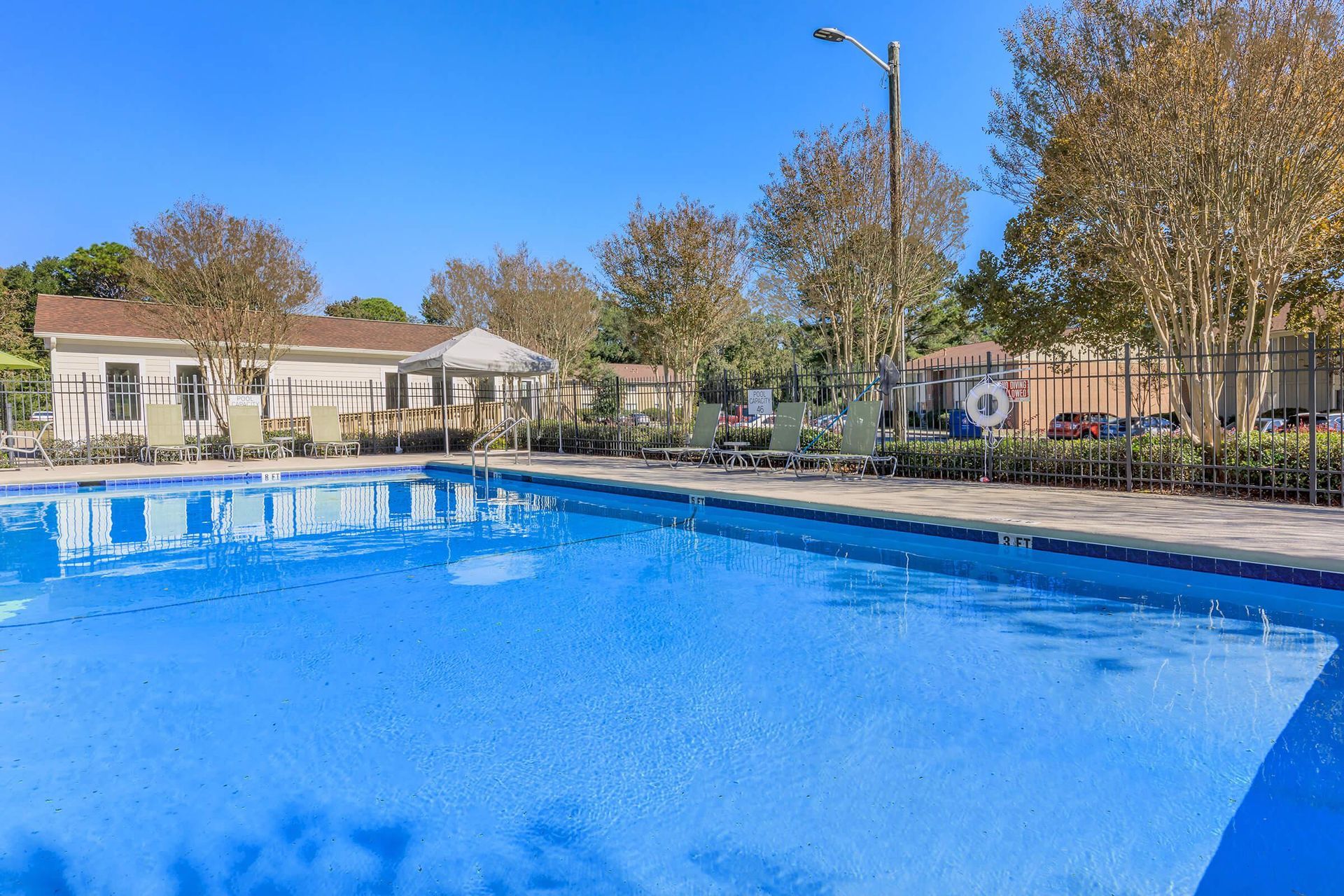 A rectangular outdoor swimming pool on a sunny day with buildings and trees in the background.