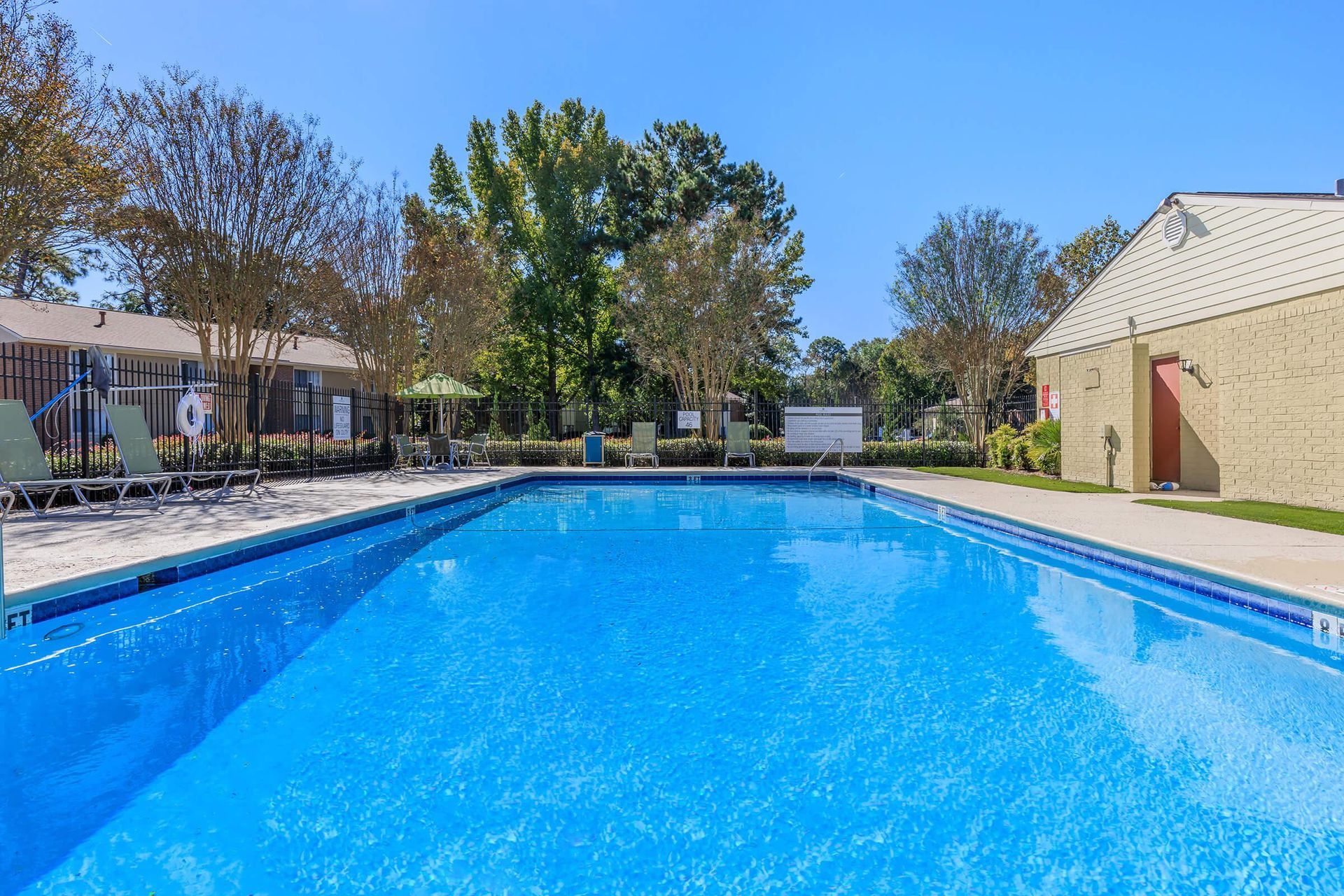 Playground with slides and climbing structures, surrounded by red mulch, against a backdrop of trees and buildings.