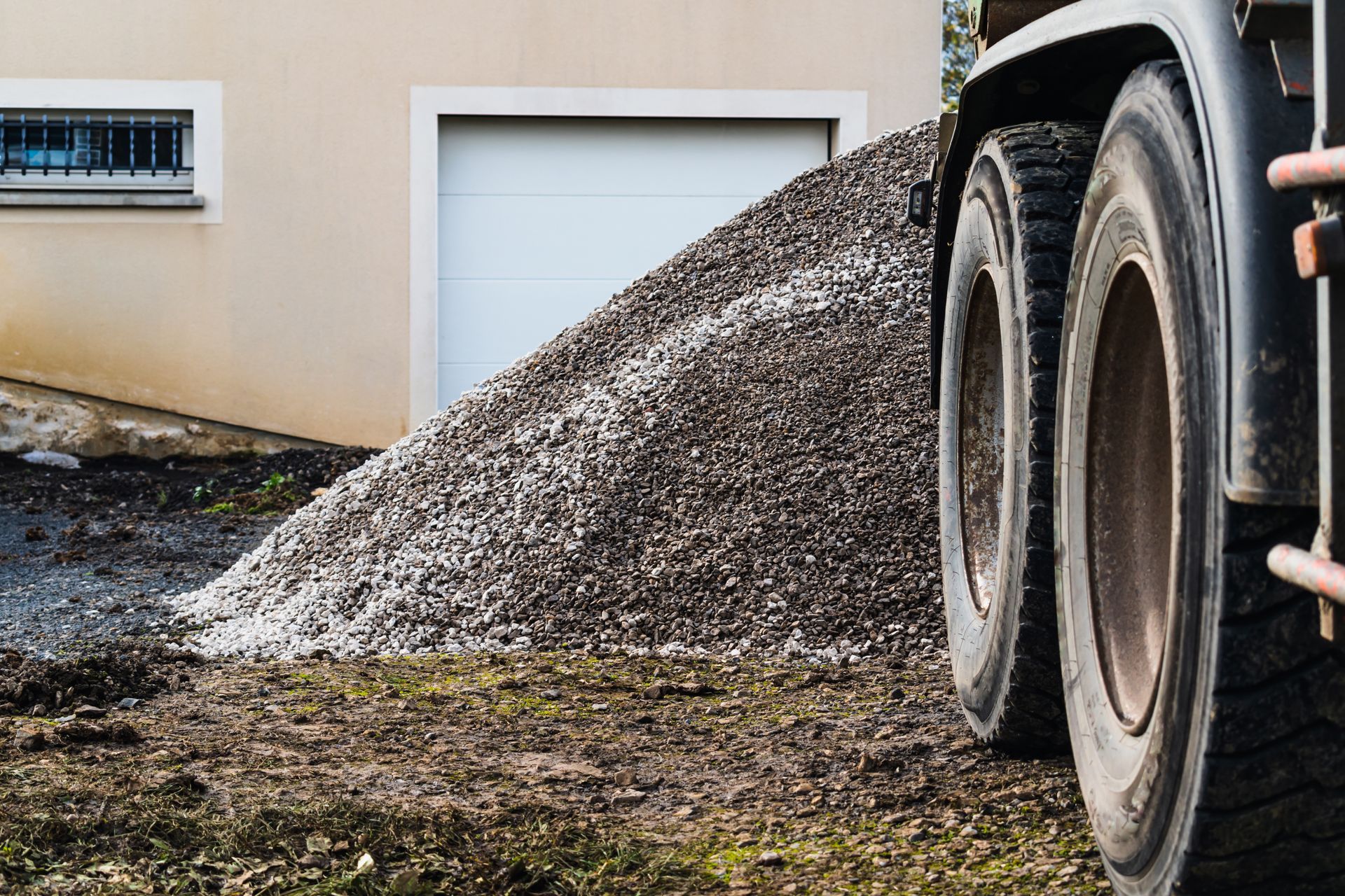 Gravel pile next to a house and garage, being delivered by a truck.
