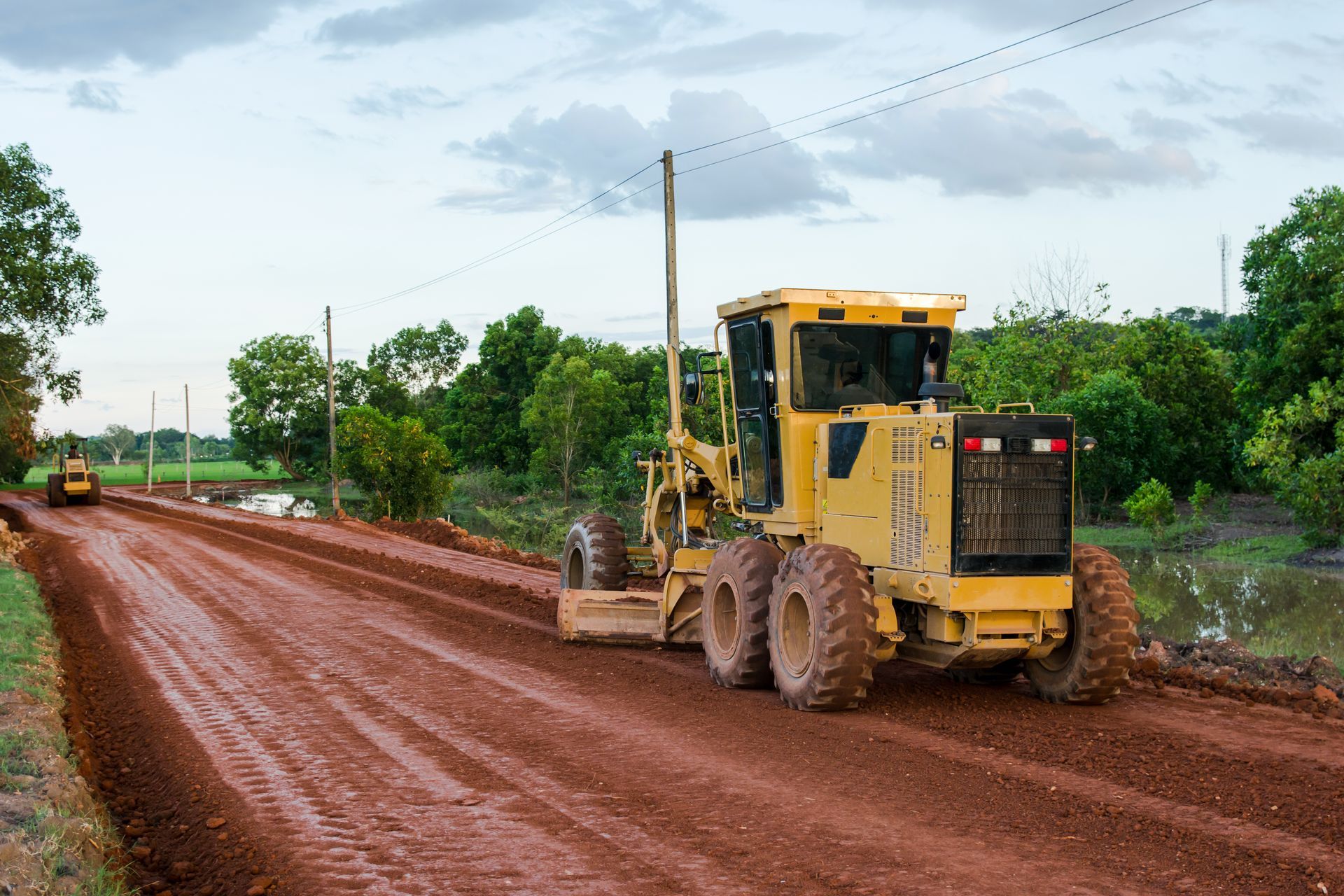 A yellow tractor is driving down a dirt road.