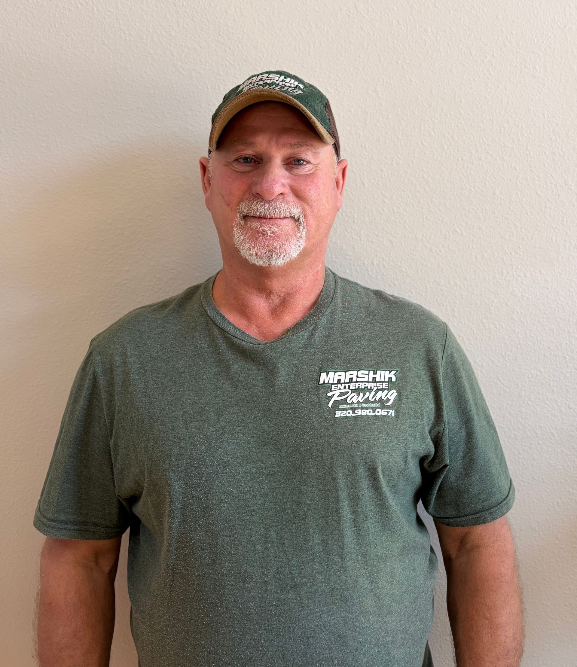 A person wearing a green Marshik Towing t-shirt and matching cap, standing against a plain light-colored wall.