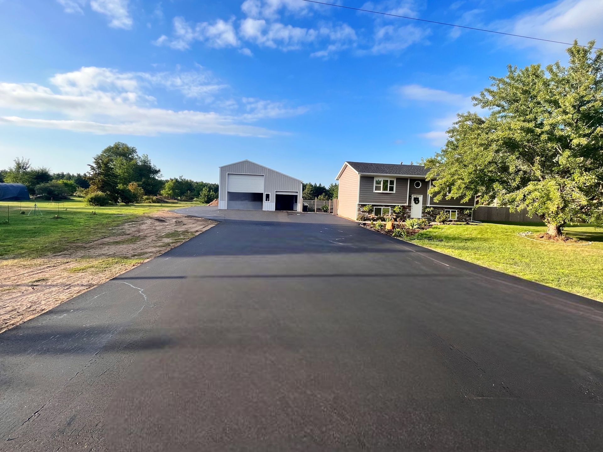 Newly paved asphalt driveway leading to a garage and house under a blue sky.