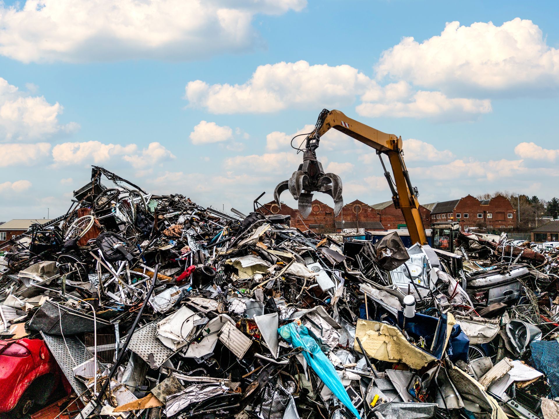 An excavator on top of a pile of scrap metal in a scrap yard. An excavator on top of a pile of scrap metal in a scrap yard.