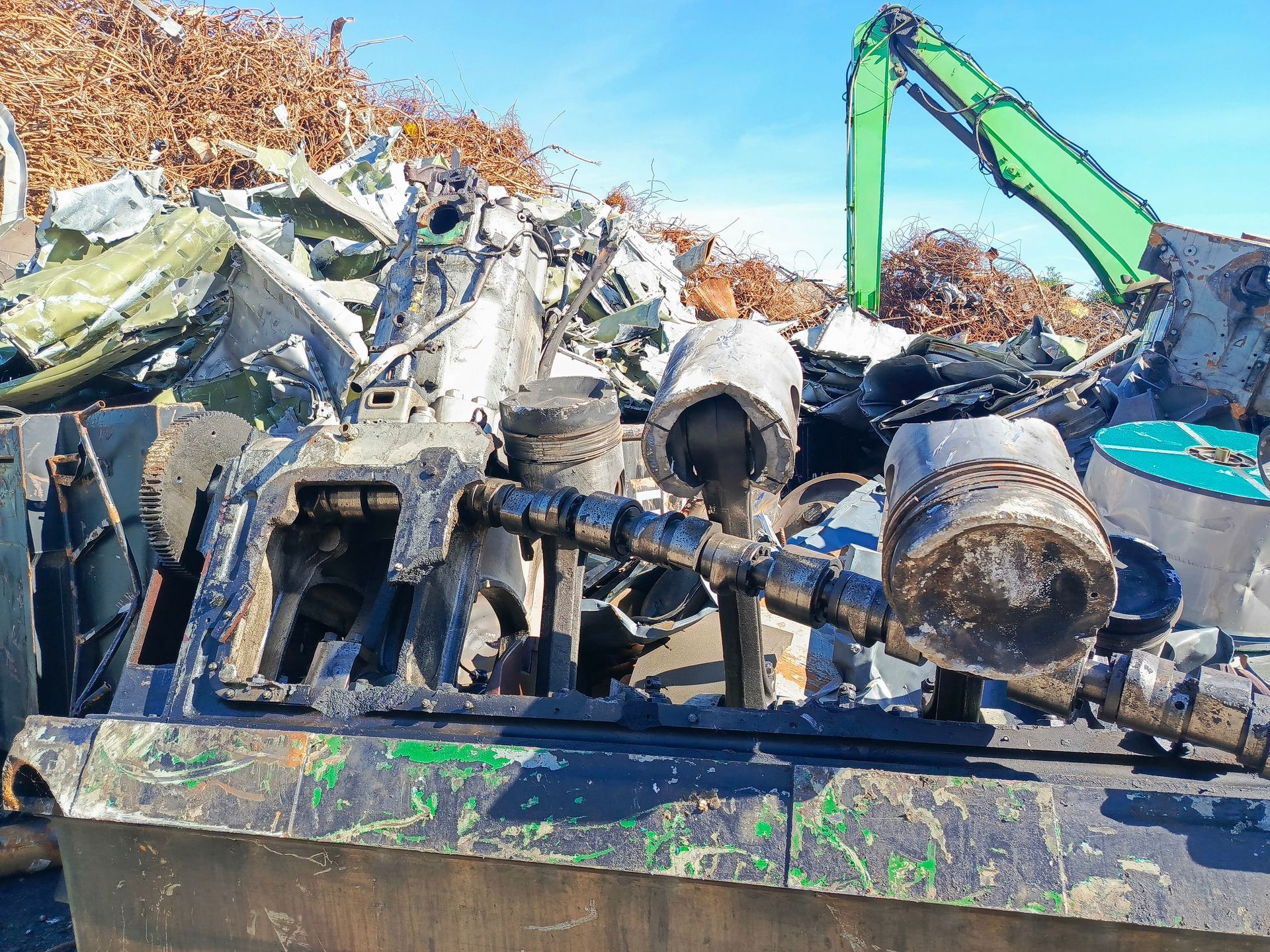 Large broken engine parts in a junkyard with other scrap metal and debris.