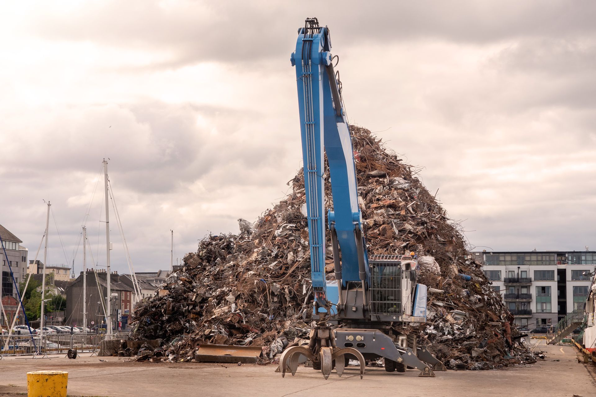 Blue excavator with a claw arm in a scrap metal yard with a pile of scrap metal behind it. Blue excavator with a claw arm in a scrap metal yard with a pile of scrap metal behind it.