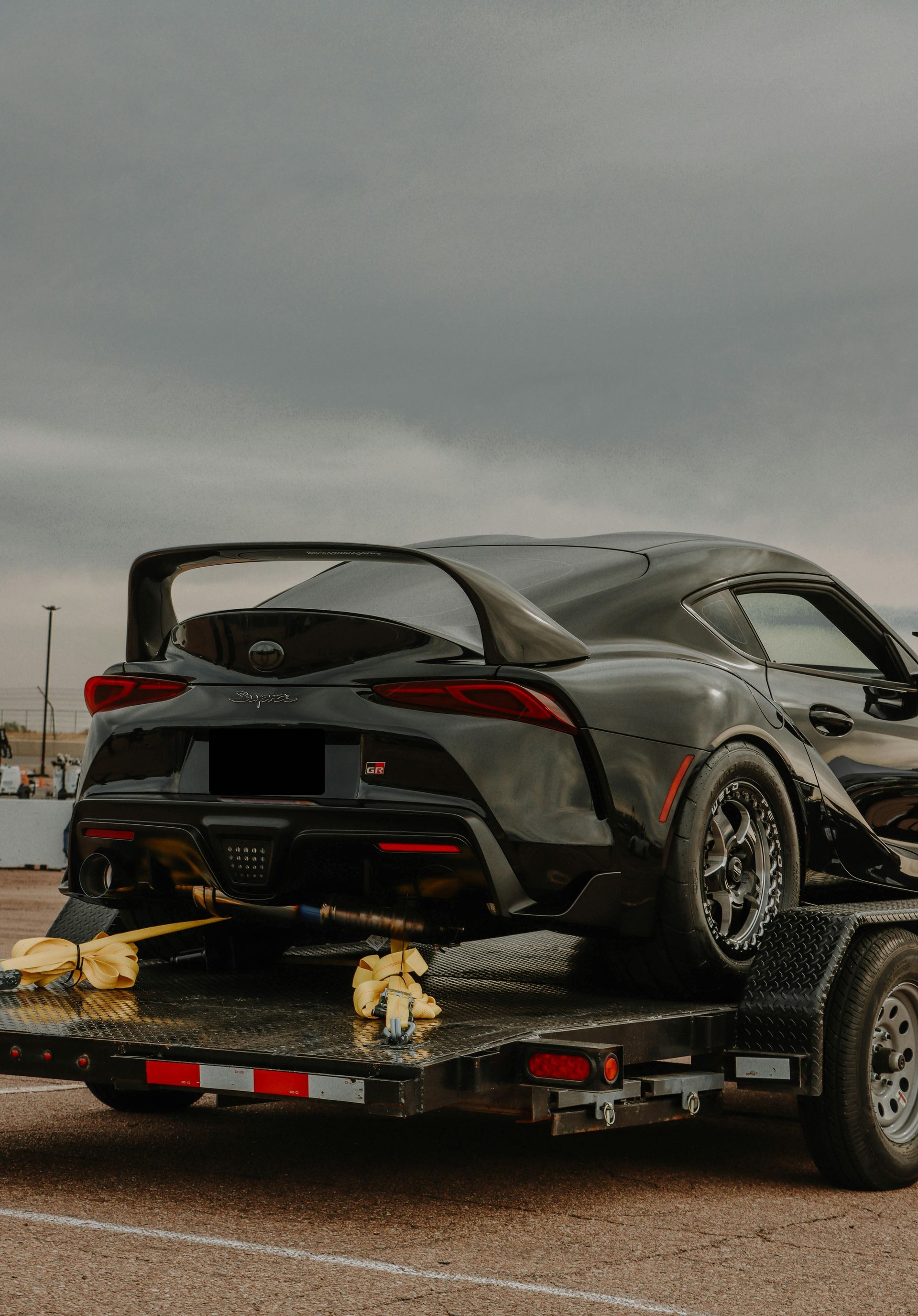 Black Toyota Supra sports car on a trailer at a racetrack under a cloudy sky. — Geelong Accident Towing & Recovery Centre In North Geelong, VIC