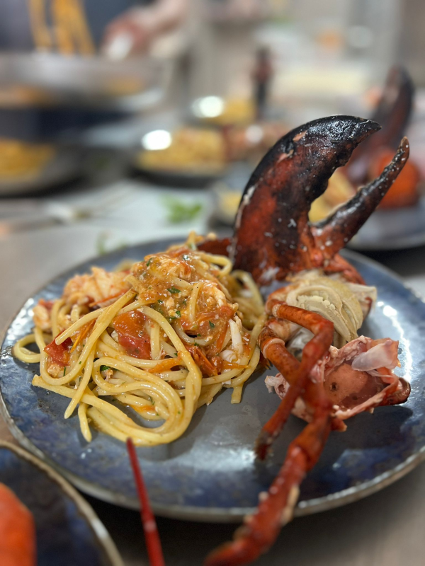 Pasta ai frutti di mare con gamberi, cozze, polpo, pomodori ed erbe aromatiche su un piatto bianco.
