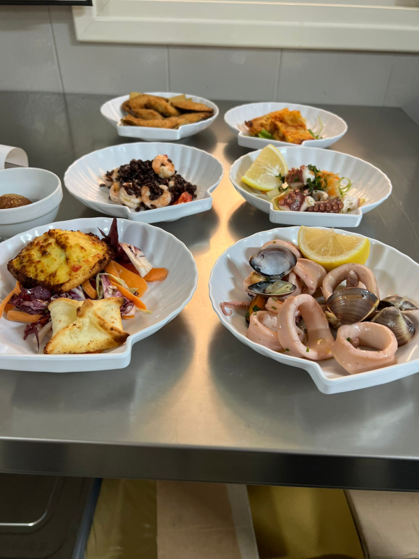 Piatto di frutti di mare con limoni e arance su un tavolo; bottiglie e bicchiere di vino sullo sfondo.