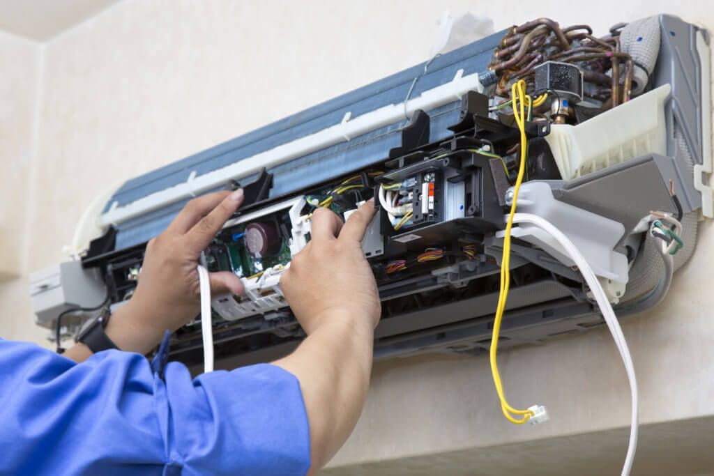 Technician repairing a wall-mounted air conditioner with exposed wiring and panels removed