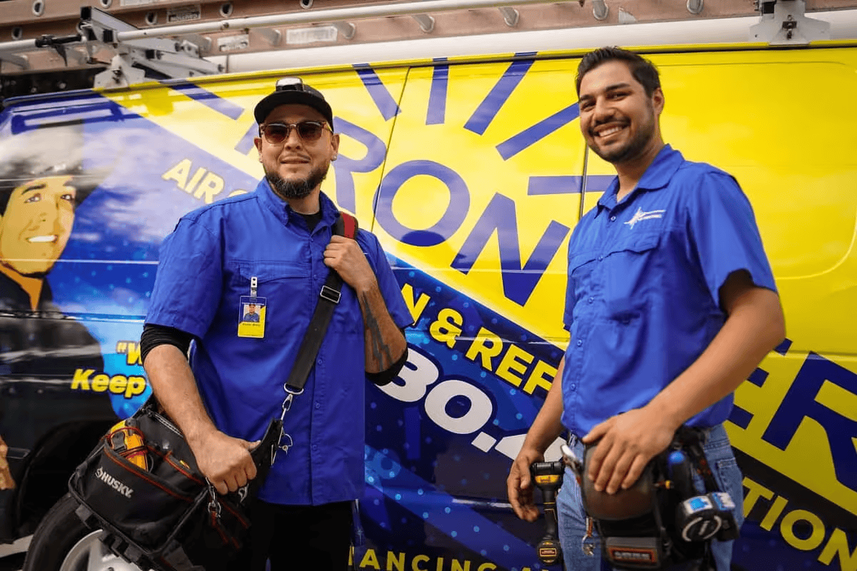 Two men in blue shirts standing in front of a colorful promotional display.