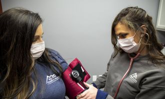 Two masked women examining a small red device indoors