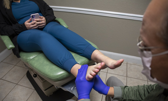 Patient’s foot being examined by a clinician in blue gloves in a medical room