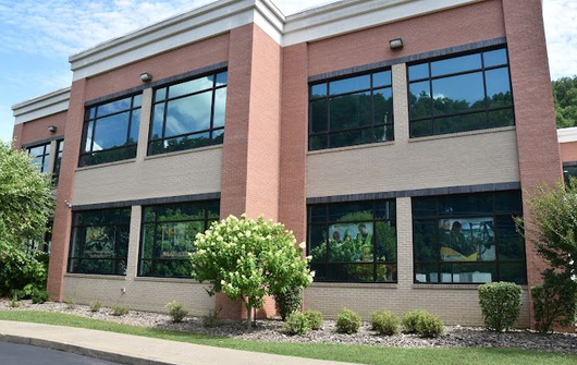 Two-story brick office building with large windows and landscaped shrubs