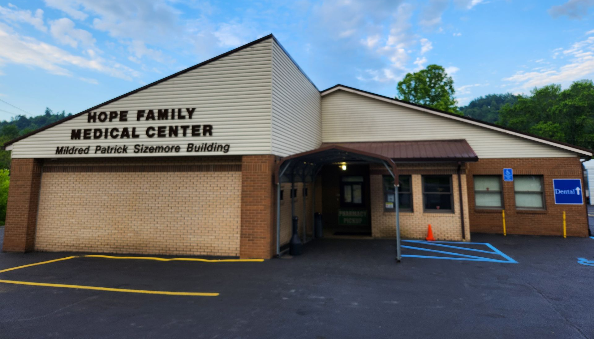 Brick building entrance with covered porch, parked car, and wooded hillside in the background