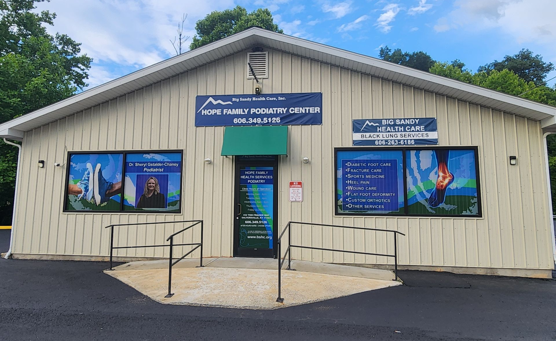 Small beige visitor center with blue signs and posters, set against trees and a cloudy sky.