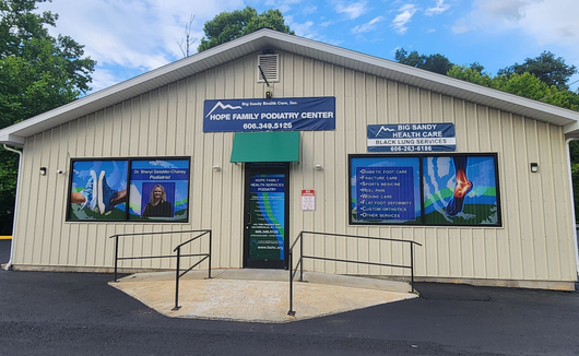 Small beige visitor center with blue signs and posters, set against trees and a cloudy sky.