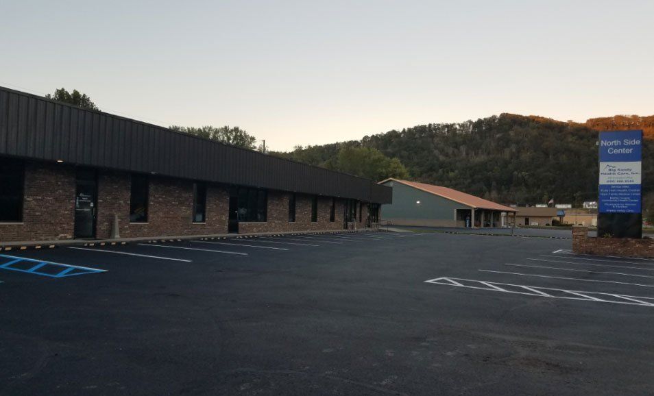 Empty parking lot beside a low brick building at dusk, with hills in the background.