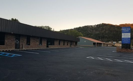 Empty parking lot beside a low brick building at dusk, with hills in the background.