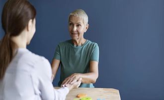 Two people talking across a table, one smiling in a green shirt against a blue wall.