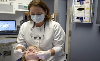 Dentist examining a patient in a dental clinic, wearing a mask and gloves.