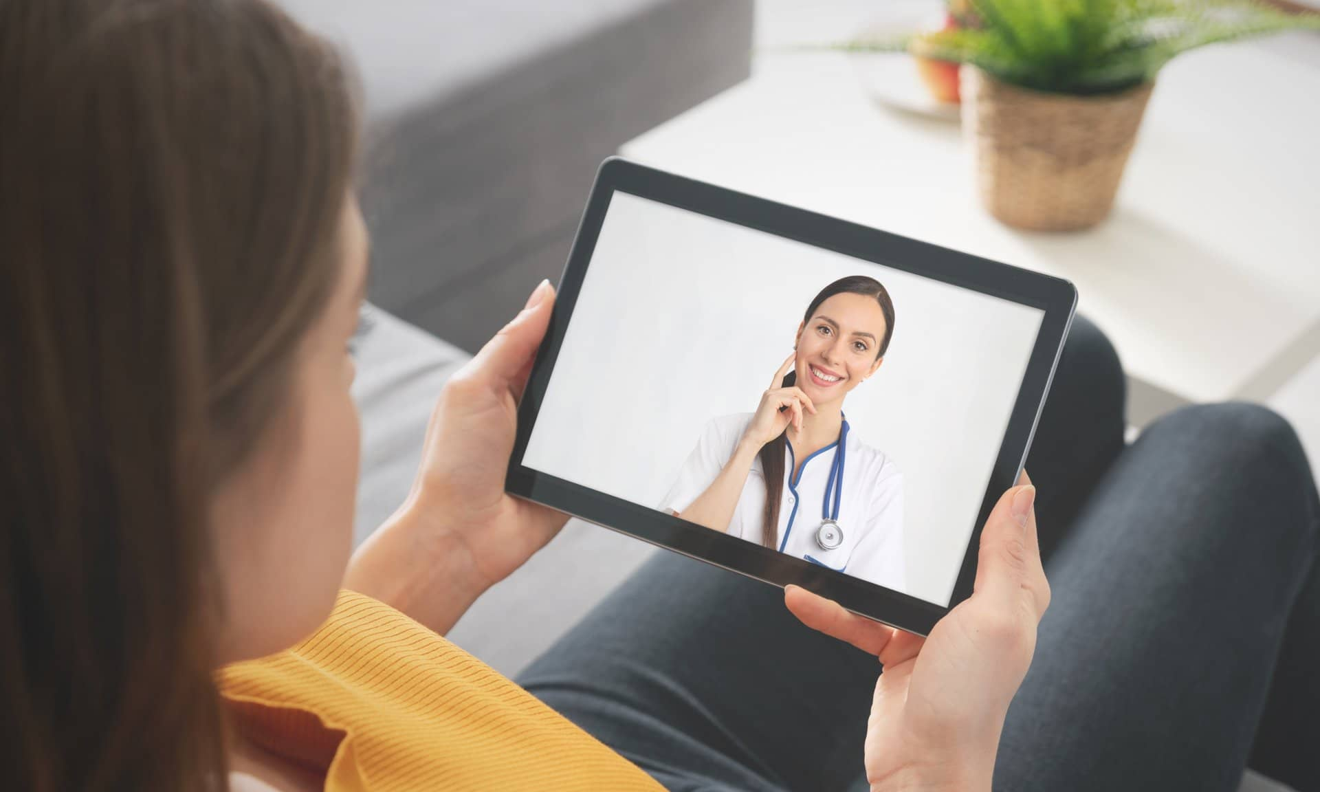 Person video chatting with a doctor on a tablet while sitting on a couch