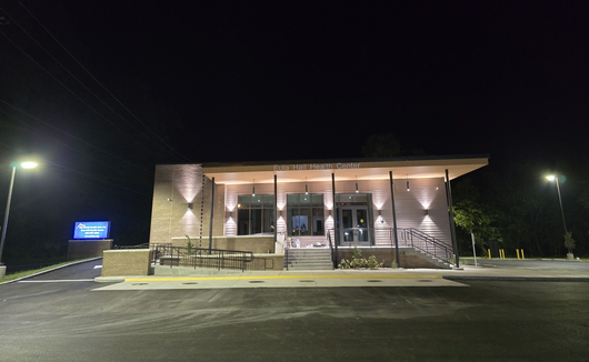 Illuminated modern building at night with columns, stone facade, and empty parking lot