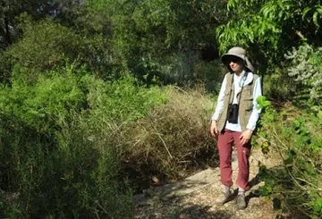 A man wearing a hat and a vest is standing in the woods.