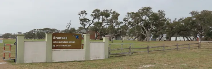 A sign on a fence in a field with trees in the background.