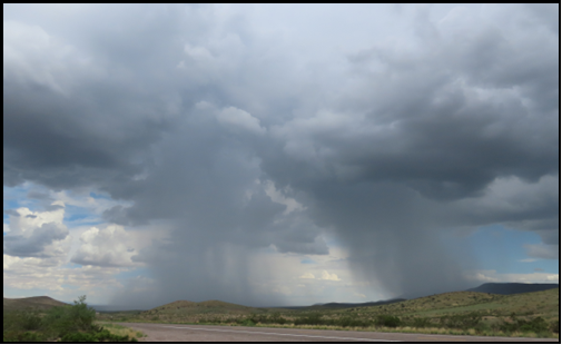 A storm is coming in over a desert landscape with mountains in the background.