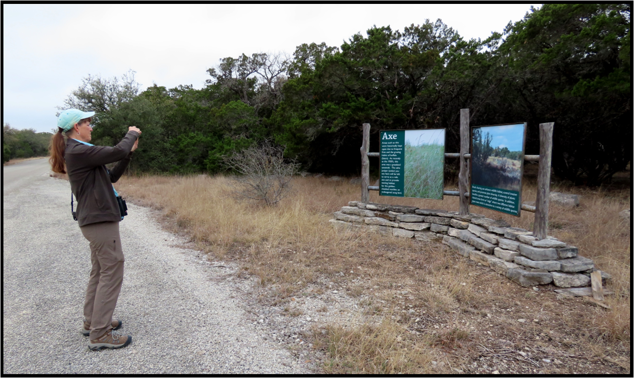 A woman is taking a picture of a sign on a dirt road.