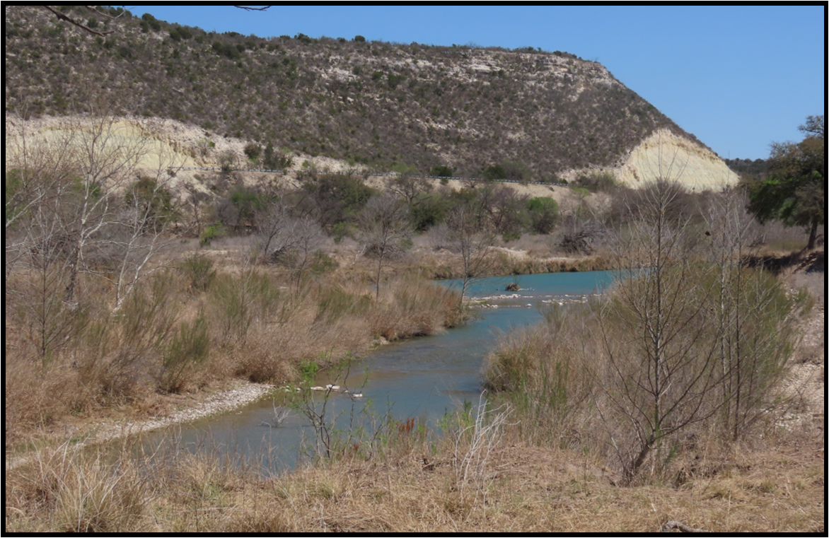 A river flowing through a dry grassy area with mountains in the background