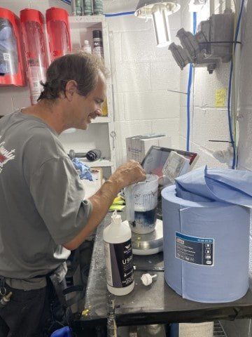 A man is standing at a counter with a bottle of liquid and a roll of paper towels.
