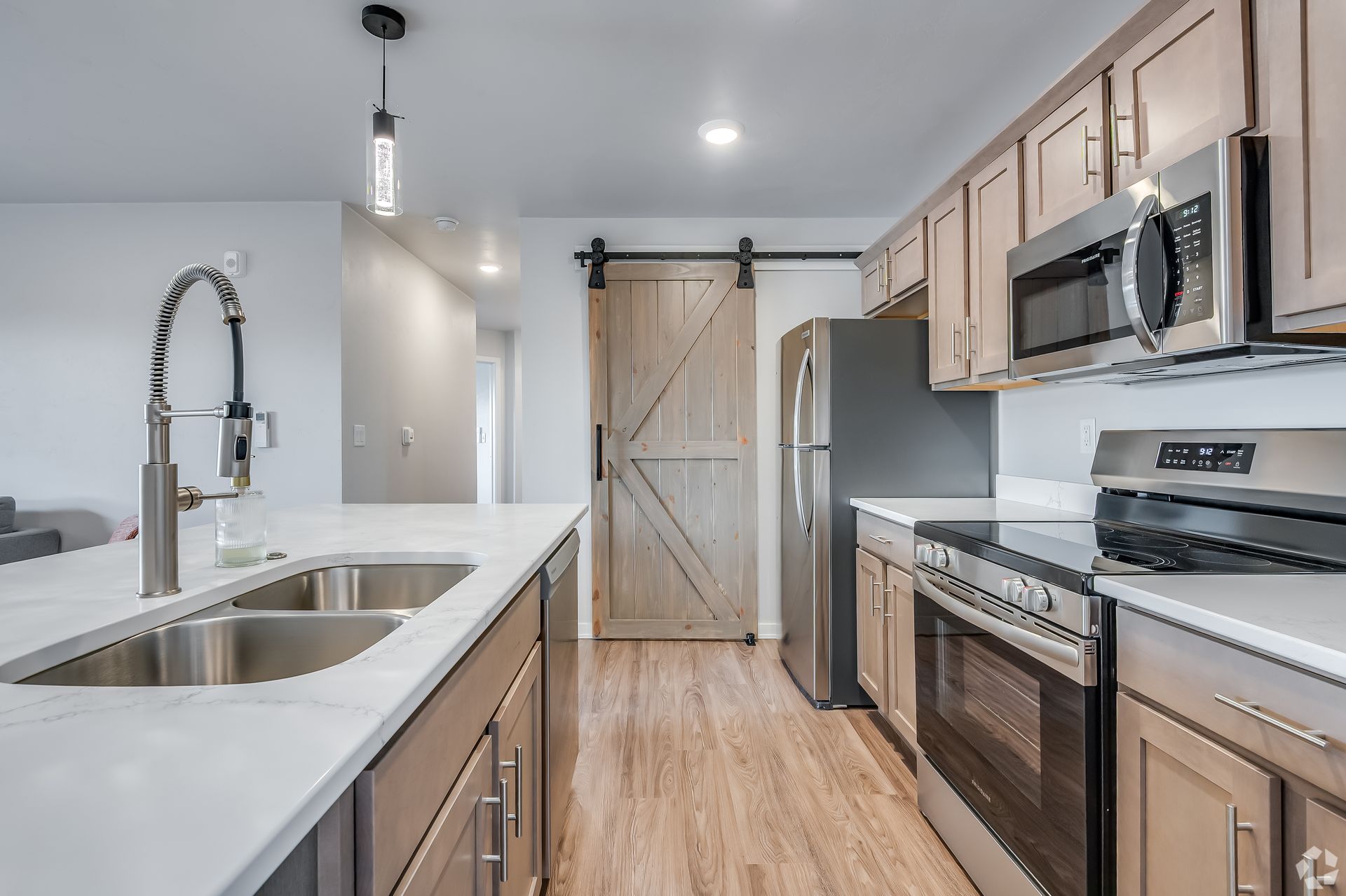 Modern kitchen with white island, stainless appliances, wood floors, and barn-style pantry door