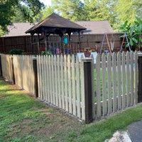 A wooden picket fence surrounds a gazebo in a backyard.